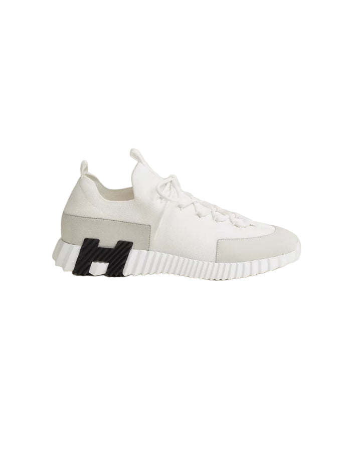 White and gray sneaker with a black 'H' logo on a beige background